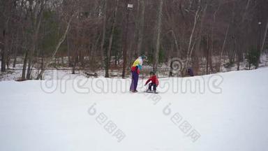 年轻人滑雪板教练教小男孩如何骑滑雪板。 冬季活动概念。 慢镜头